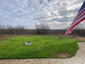 A grassy field with a flag, trees, and a cloudy sky.