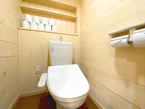 A small, compact bathroom with a white toilet, a shelf with toilet paper, and a wall-mounted toilet paper holder.