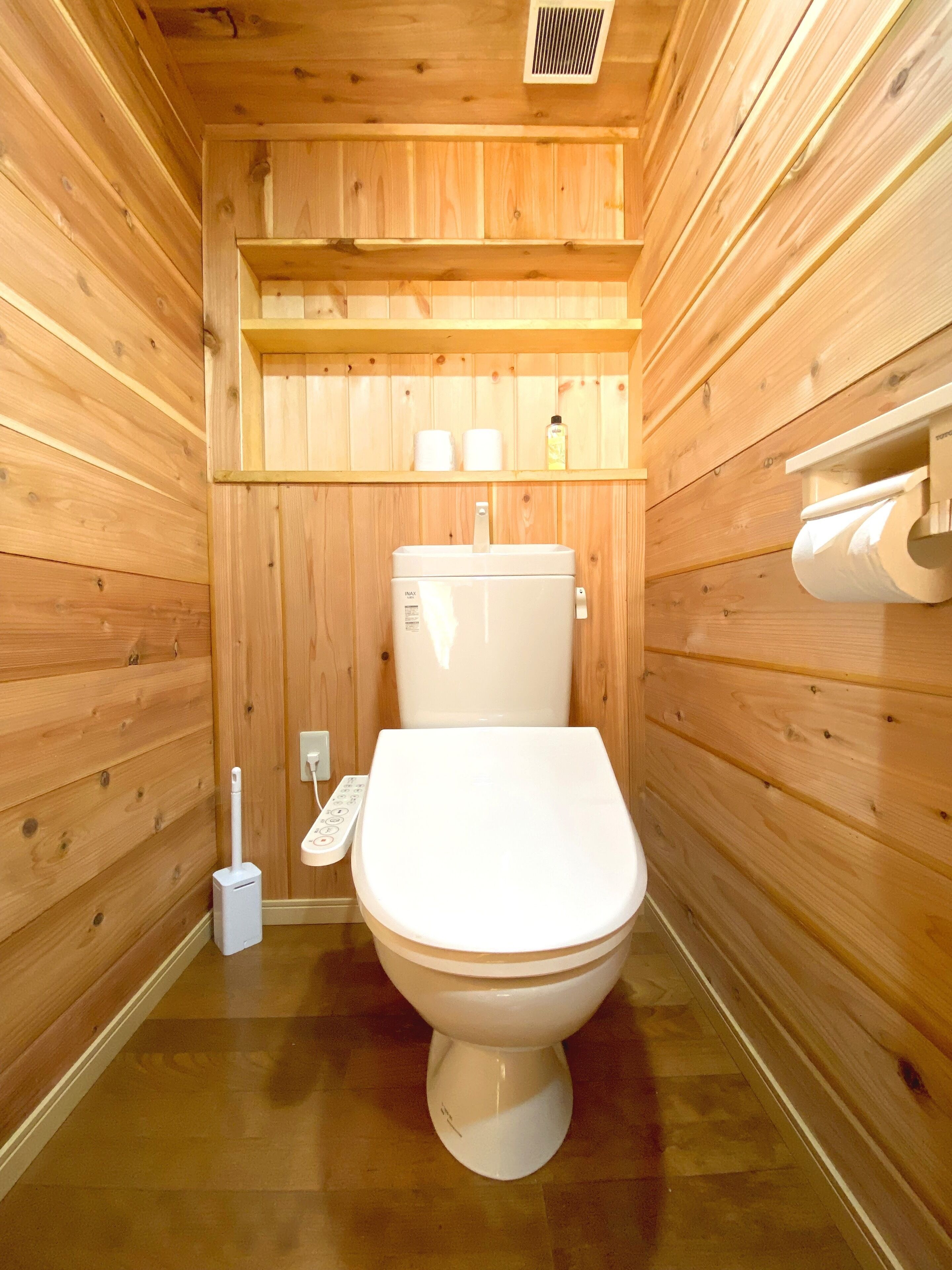 A wooden cabin bathroom with a toilet, a hand dryer, and a shelf with toiletries.