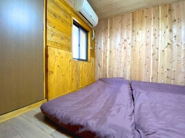 Quarto com paredes de madeira, uma janela e uma cama com colchão roxo.