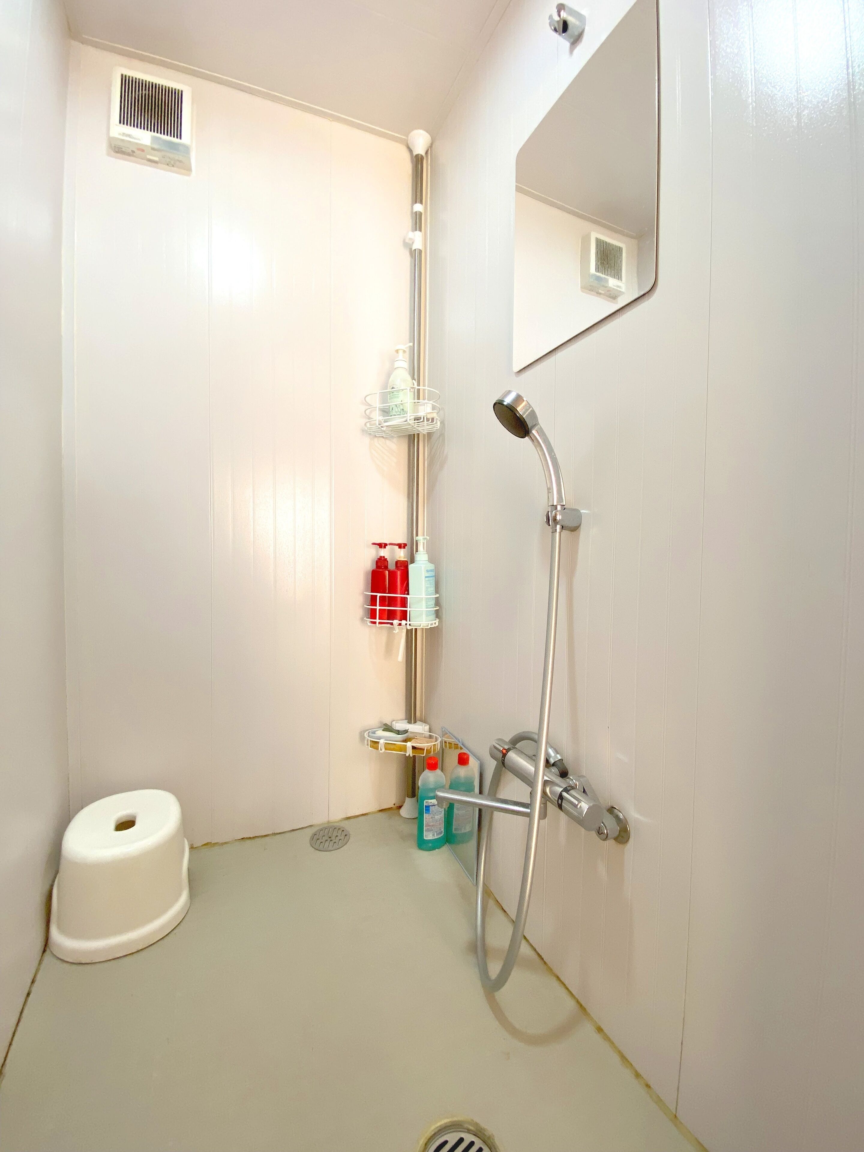 A small, white bathroom with a shower, toilet, and storage shelves.