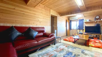A cozy cabin interior with a red leather sofa, a wooden table, and a patterned rug.