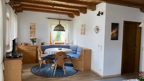 Et hyggeligt rum med træloft, et rundt bord med stole, en blå sofa og et vindue med gardiner.