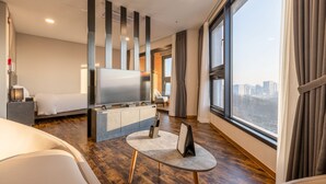 Ein modernes Hotelzimmer mit einem großen Bett, einem Fernseher, einem kleinen Tisch und Blick auf die Stadt durch große Fenster.