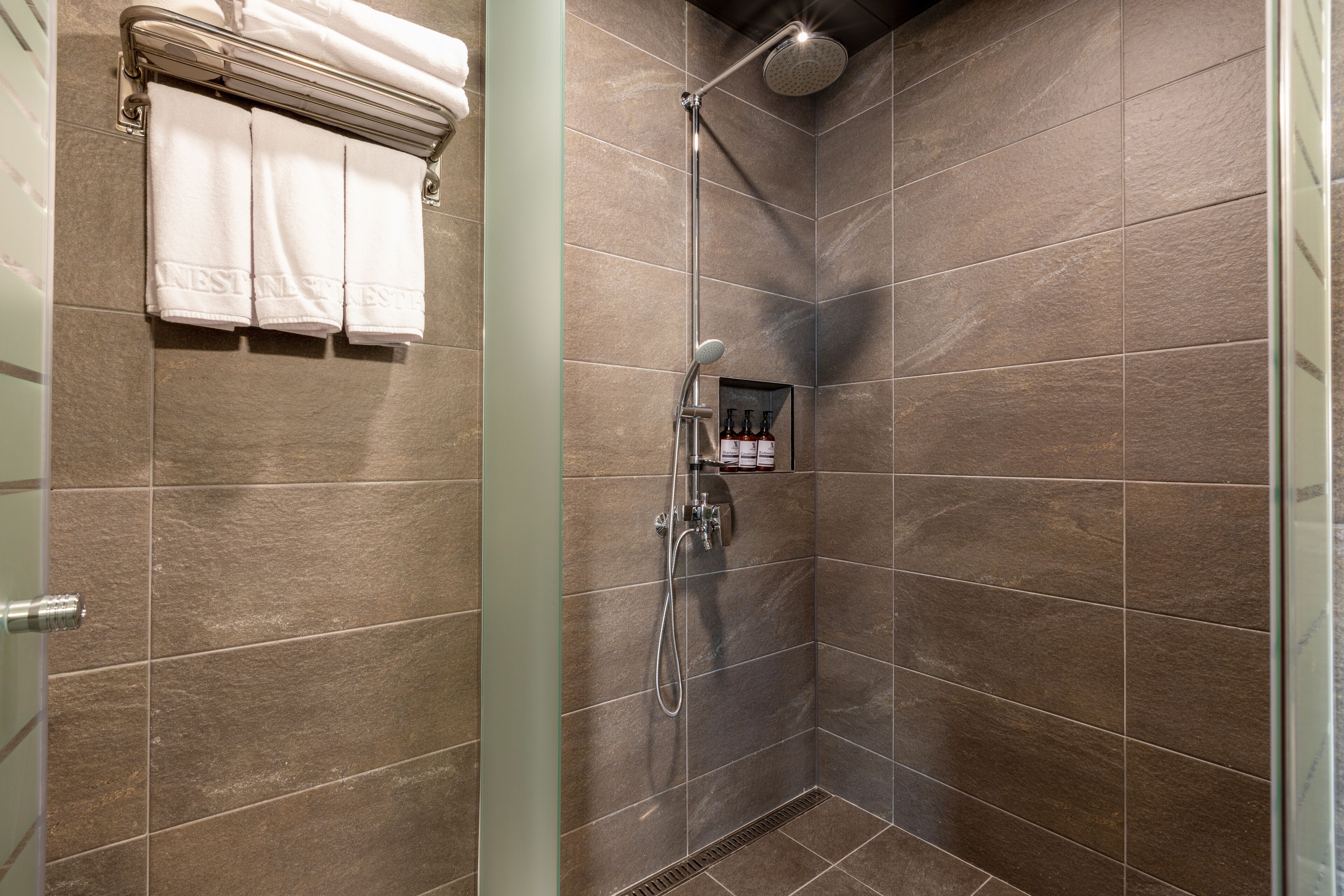 A shower area with a glass door, a towel rack with three towels, and a showerhead.