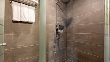 A shower area with a glass door, a towel rack with three towels, and a showerhead.