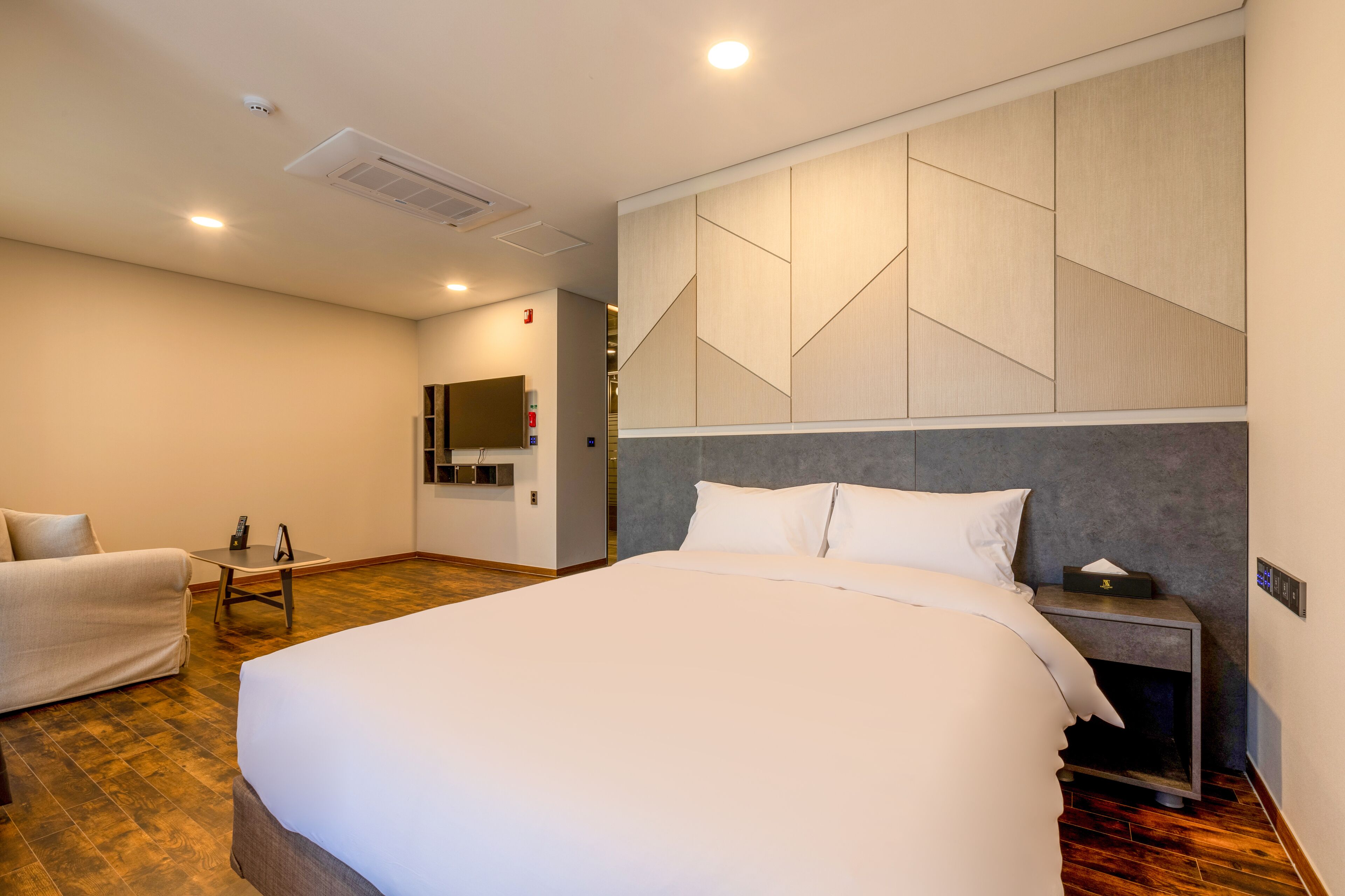 Ein Hotelzimmer mit einem großen Bett, einem Nachttisch, einem Sessel und Holzboden.