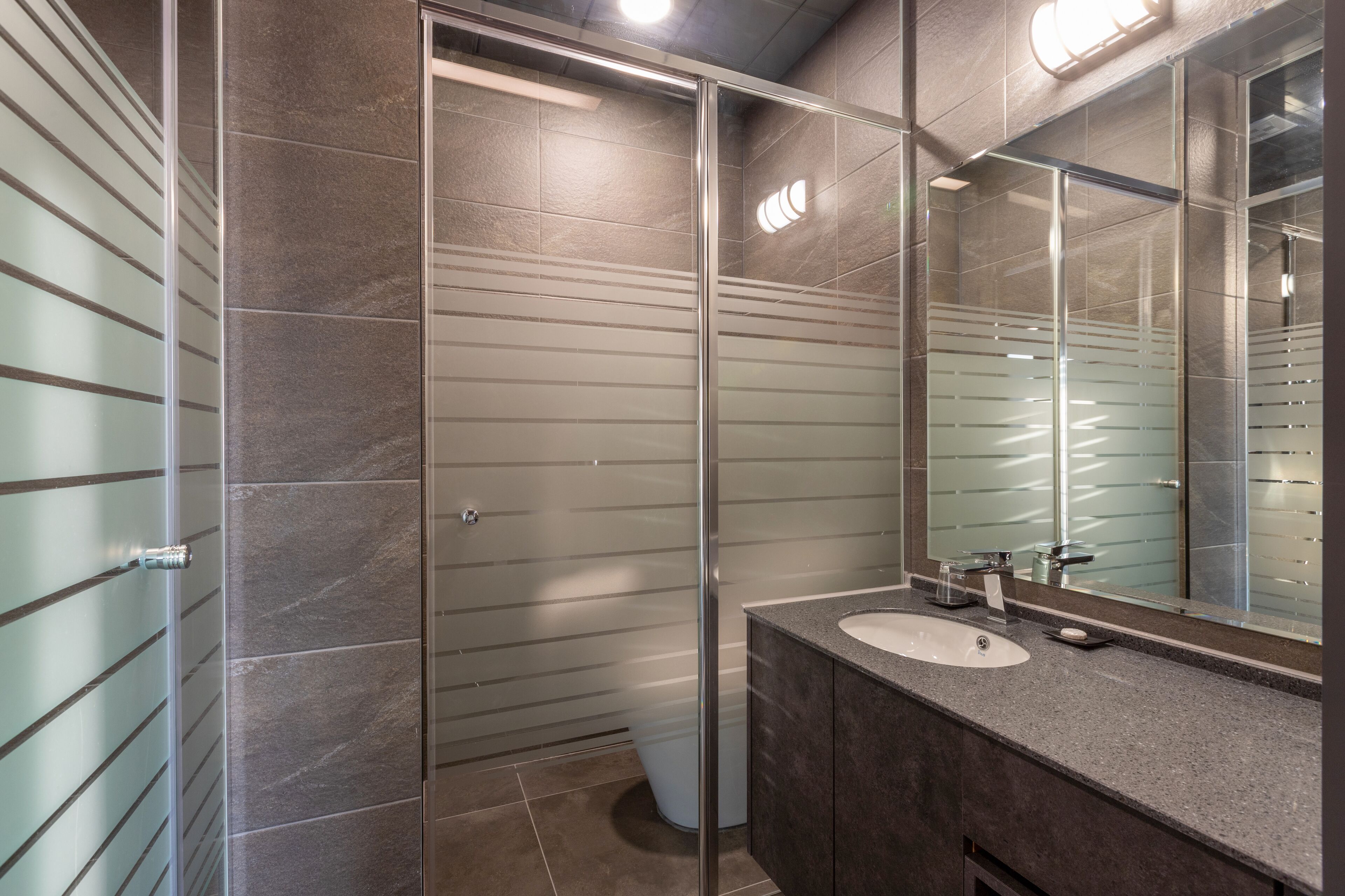 A modern bathroom with a glass shower enclosure, a sink with a mirror, and a tiled floor.