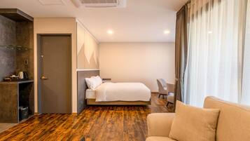 A hotel room with a wooden floor, a bed, a sofa, a desk, and a window with curtains.