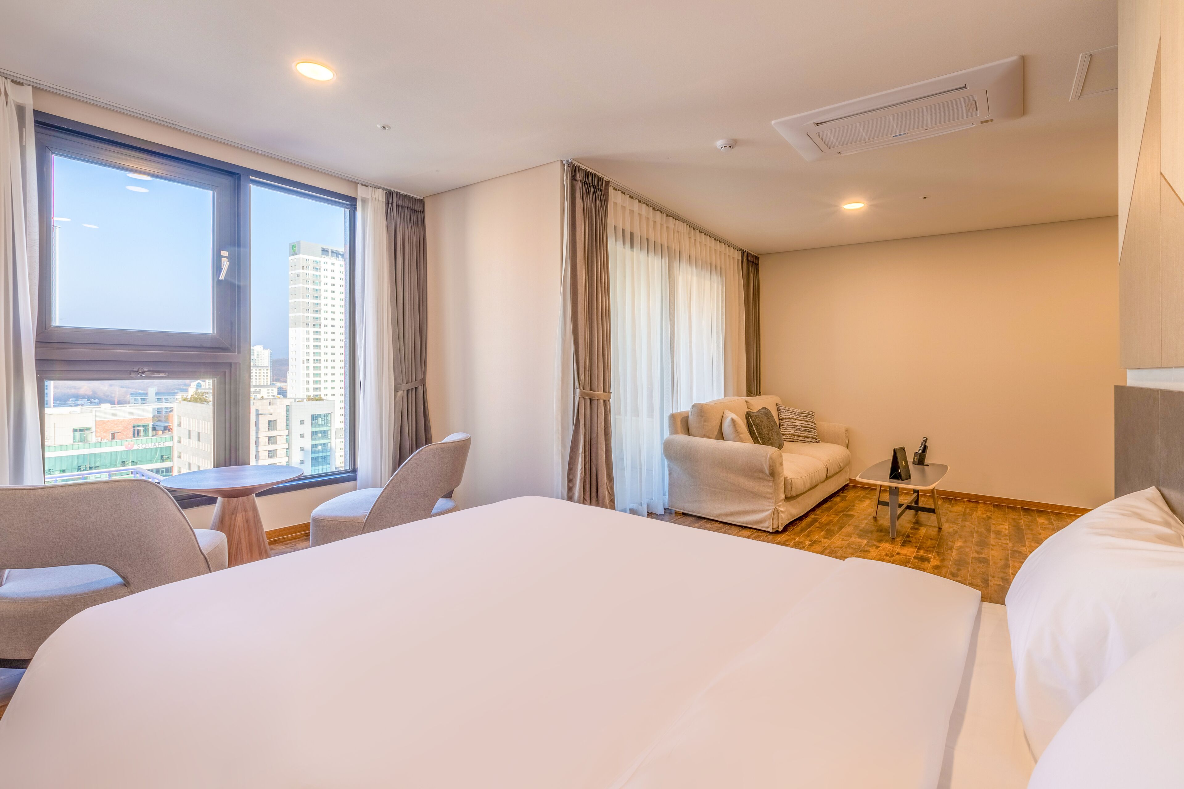 Une chambre d’hôtel avec un grand lit, un canapé, une petite table et une fenêtre avec des rideaux.