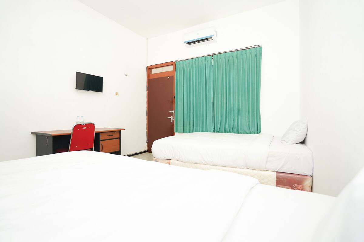 A hotel room with a bed, a desk, a chair, a TV, and a door.