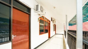 A corridor with a red door, a window with a metal grill, and an air conditioning unit mounted on the wall.