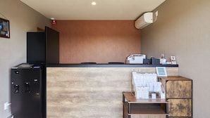 A reception area with a wooden counter, a black service desk, a cash register, and a small wooden cabinet. - HOTEL R9 The Yard Higashiomi (Higashiomi)