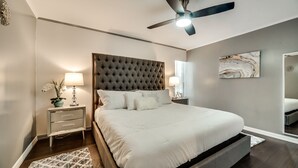 A bedroom with a tufted headboard, a bed with white bedding, a nightstand with a lamp, and a ceiling fan. - 1st Flr Luxury2b 2bth Condo w/King/2 sep twin beds (Grand Prairie)