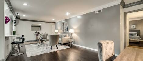 A spacious living room with dark wood flooring, a grey accent wall, and a dining area with a wooden table and chairs.