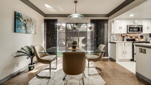 A modern kitchen with white cabinets, a stainless steel microwave, and a dining area with a glass table and two chairs. - 1st Flr Luxury2b 2bth Condo w/King/2 sep twin beds (Grand Prairie)