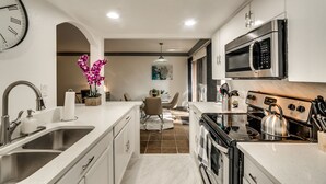 A modern kitchen with stainless steel appliances, a sink, and a dining area with a table and chairs. - 1st Flr Luxury2b 2bth Condo w/King/2 sep twin beds (Grand Prairie)