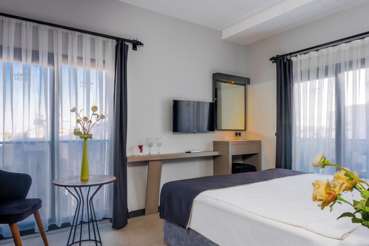 Ein Hotelzimmer mit Bett, Schreibtisch, Fernseher und einem Fenster mit Vorhängen.