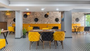 A modern dining area with brick walls, yellow and black upholstered chairs, and a patterned floor.