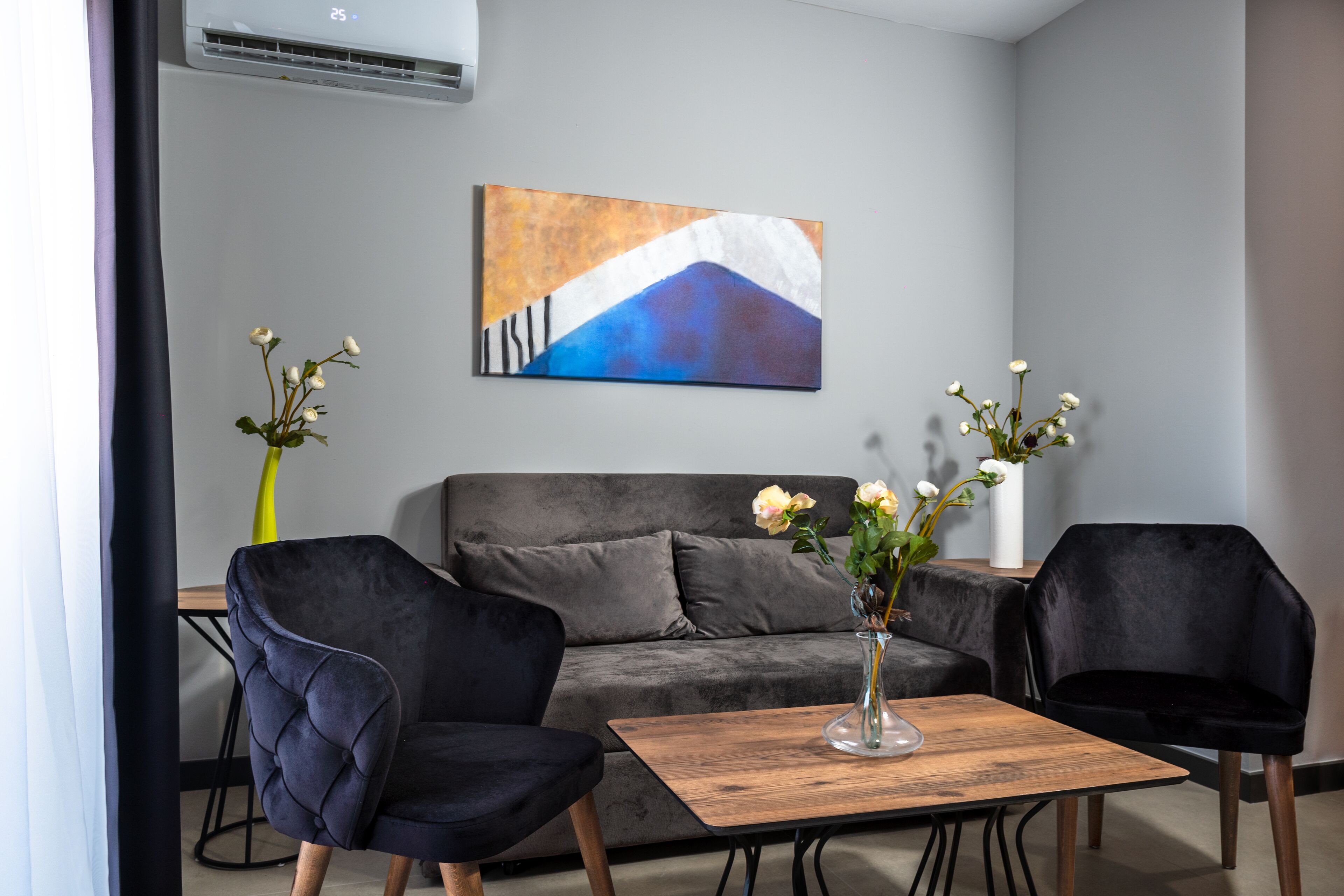 A modern living room with a grey sofa, two black armchairs, a wooden coffee table, and a vase with flowers.