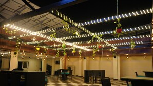 Un restaurante con piso de cuadros, mesas, sillas, plantas colgantes y luces de cuerda.