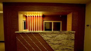 Un área de recepción con mostrador de mármol, paneles de madera y una puerta con persianas verticales.