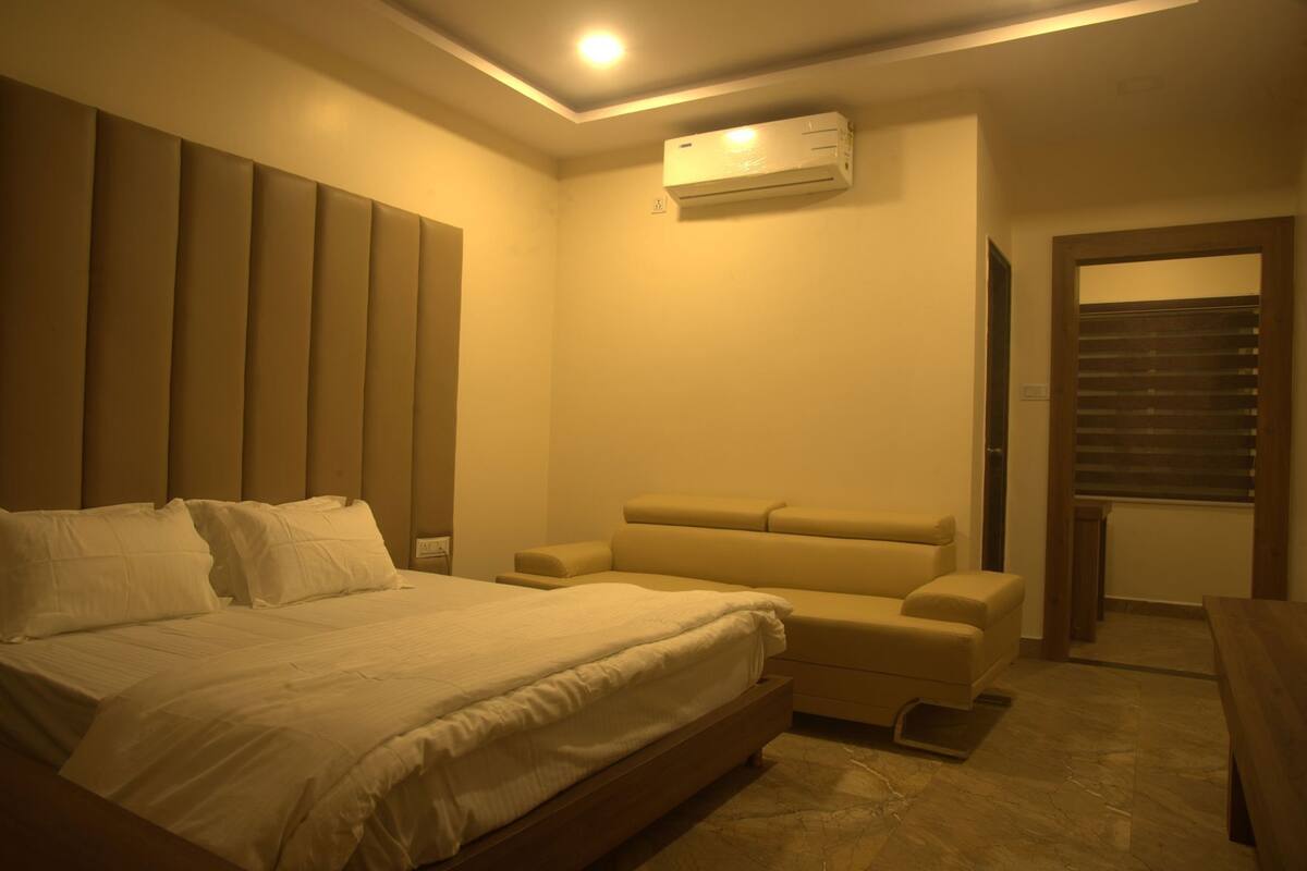 Un dormitorio con cama, sofá, aire acondicionado y puerta que da a otra habitación.