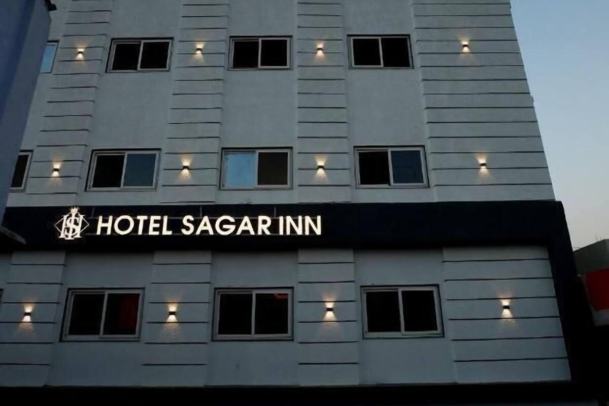 Un hotel de varios pisos con fachada moderna, ventanas iluminadas y un cartel que dice 'HOTEL SAGAR INN'.
