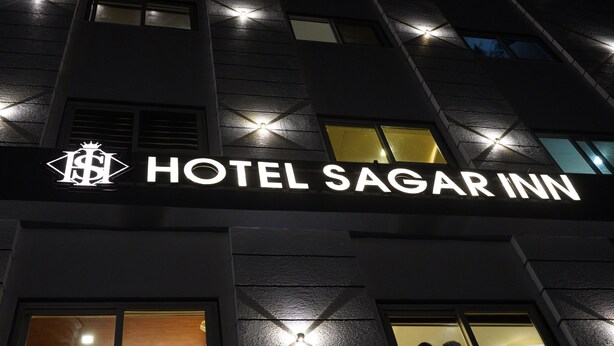 Fachada del Hotel Sagar Inn con señalización iluminada y ventanas.