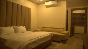 Un dormitorio con cama, un banco, un equipo de aire acondicionado y una puerta que da a otra habitación.