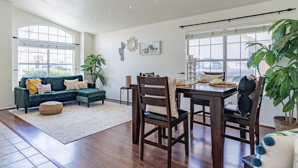 A spacious living area with a dark green sofa, a dining table with chairs, and large windows providing natural light. - ☀️🌵Tropical Desert Oasis. HEATED Pool & Spa no charge. Private, large yard 🌴🏜 (Glendale)