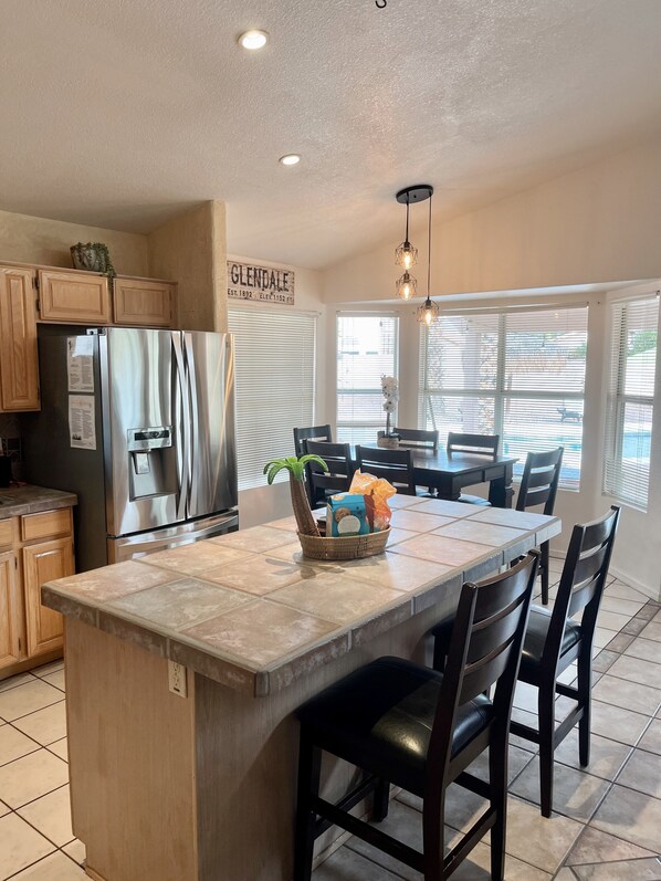 A kitchen with a central island, wooden cabinets, a stainless steel refrigerator, and a dining area with a table and chairs.