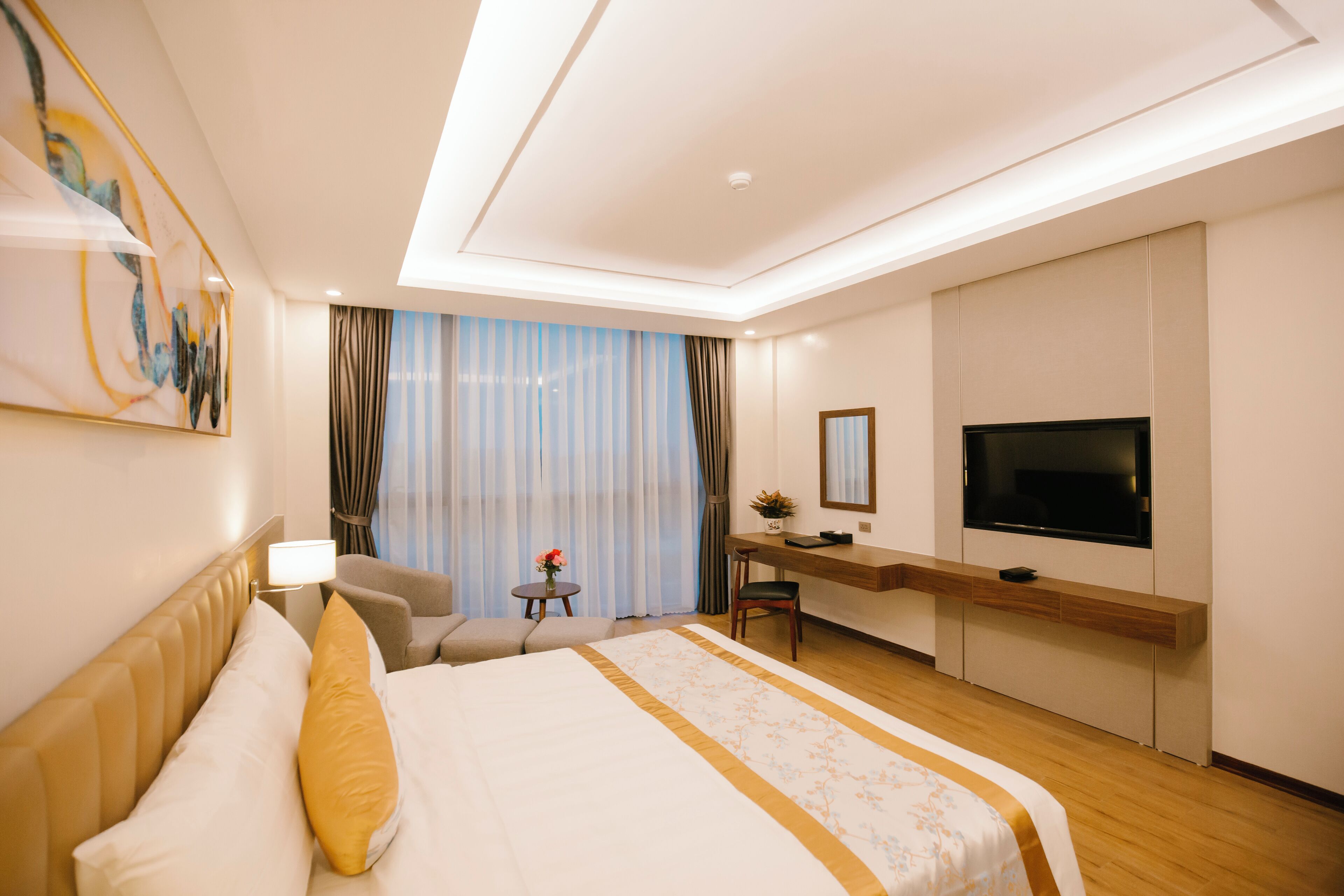 Una habitación de hotel con una cama grande, un escritorio, una silla, un televisor y una ventana con cortinas.