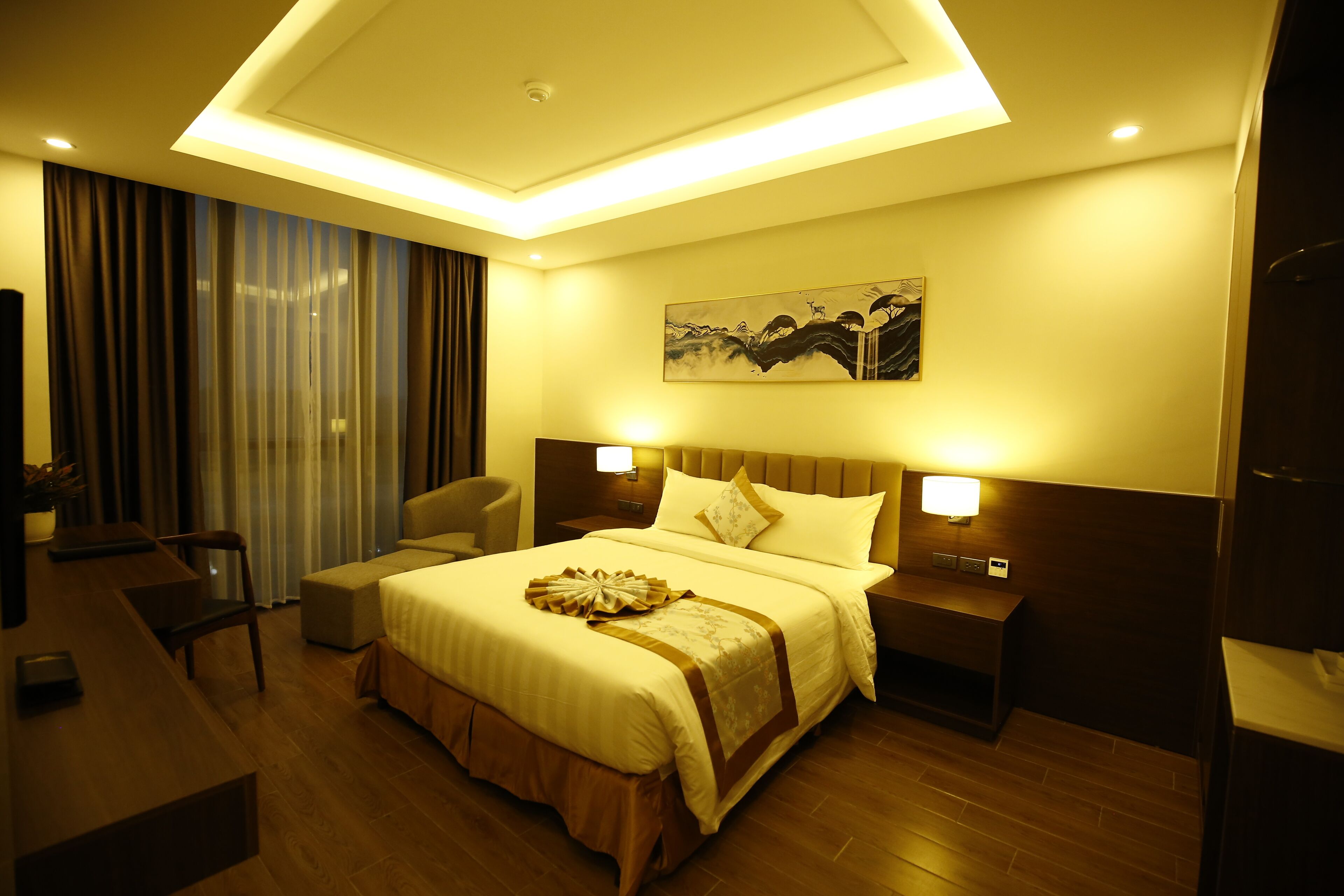 A hotel room with a large bed, bedside tables, a desk, and a chair.