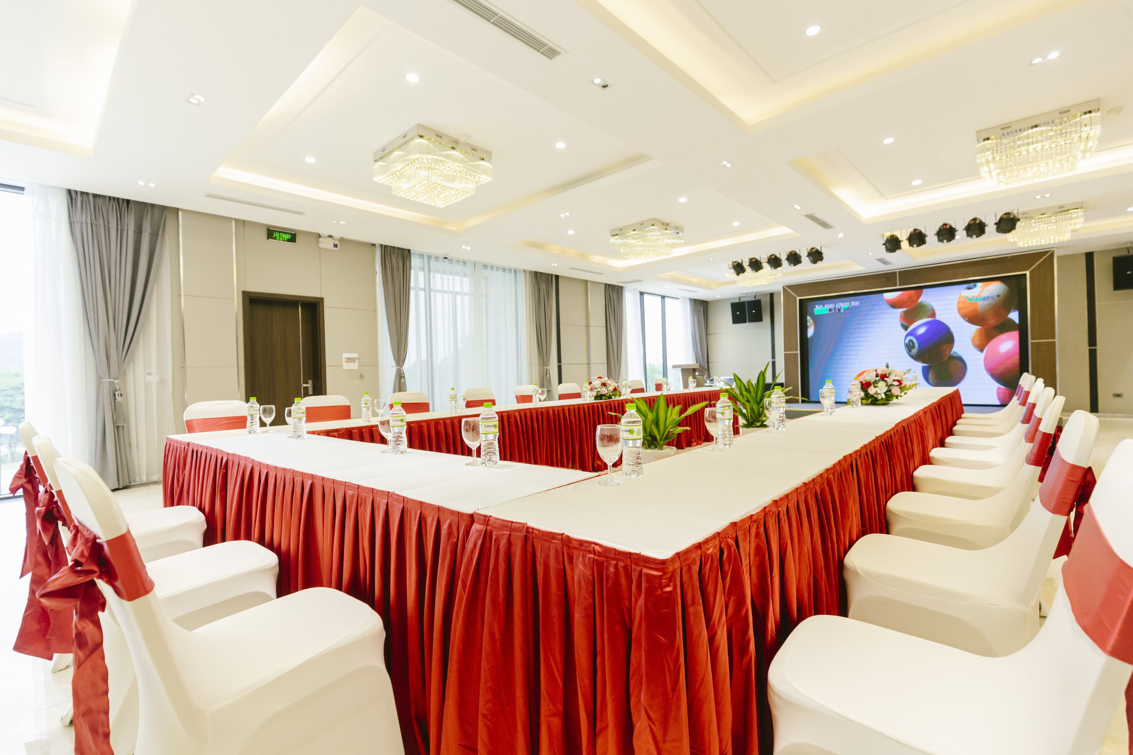 Un salón de conferencias con una mesa larga, sillas blancas y una pantalla grande.