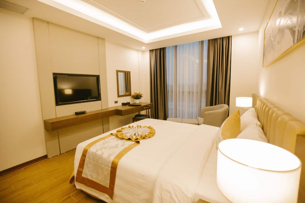 A hotel room with a large bed, a desk with a TV, a chair, and a window with curtains.