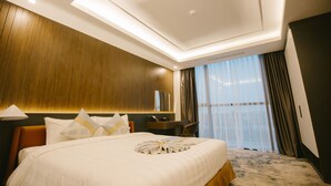 A modern hotel room with a large bed, a wooden headboard, a desk, and a large window with curtains. - Songlam Waterfront Hotel - 藍江酒店 (Nghi Xuân)