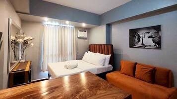 A hotel room with a bed, a wooden table, an orange sofa, a mirror, and a painting on the wall.