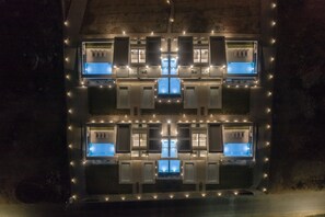 Fachada de edificio con múltiples ventanas y una piscina central, iluminada por luces colgantes.