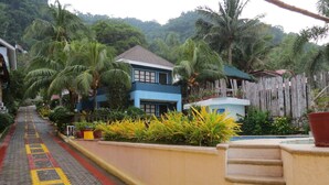 A pathway leading to a blue building with a red roof, surrounded by lush greenery and palm trees. - Pier Uno Dive Resort (Bauan)