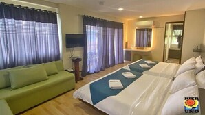 A hotel room with a bed, a green sofa, a TV, and curtains. - Pier Uno Dive Resort (Bauan)