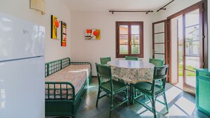Una habitación pequeña con una cama, una mesa y sillas. Se ve una ventana con vistas al exterior.
