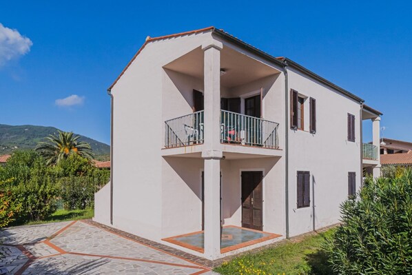 Ein zweistöckiges Haus mit Balkon, einer gefliesten Terrasse und Blick auf die umliegende Natur und Hügel.