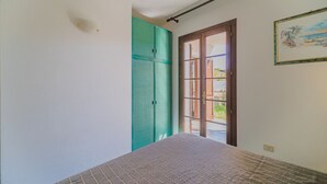 Una habitación con una cama, un armario verde y una puerta que da al exterior.