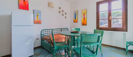 A room with a bed, a dining table with chairs, a refrigerator, and artwork on the walls.