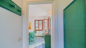 A hallway leading to a dining area with green chairs and a table, a window with a view, and a door with a green screen. - APP.TI STELLA MARINA - STELLA MARINA 4 (Marina di Campo)