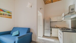 A compact living space with a kitchenette, a blue sofa, and a painting on the wall.