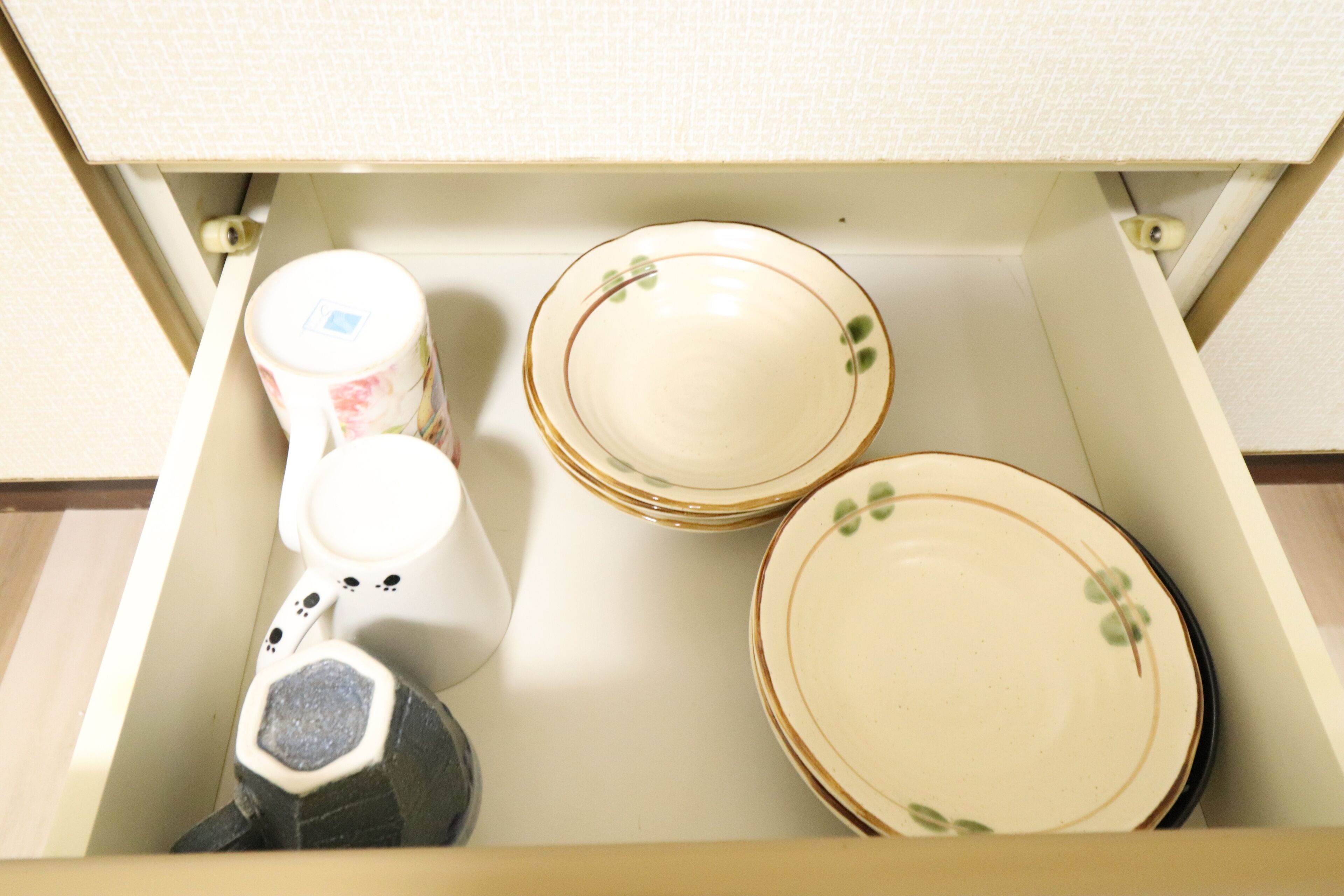 A drawer containing plates, a mug, and a hexagonal object.