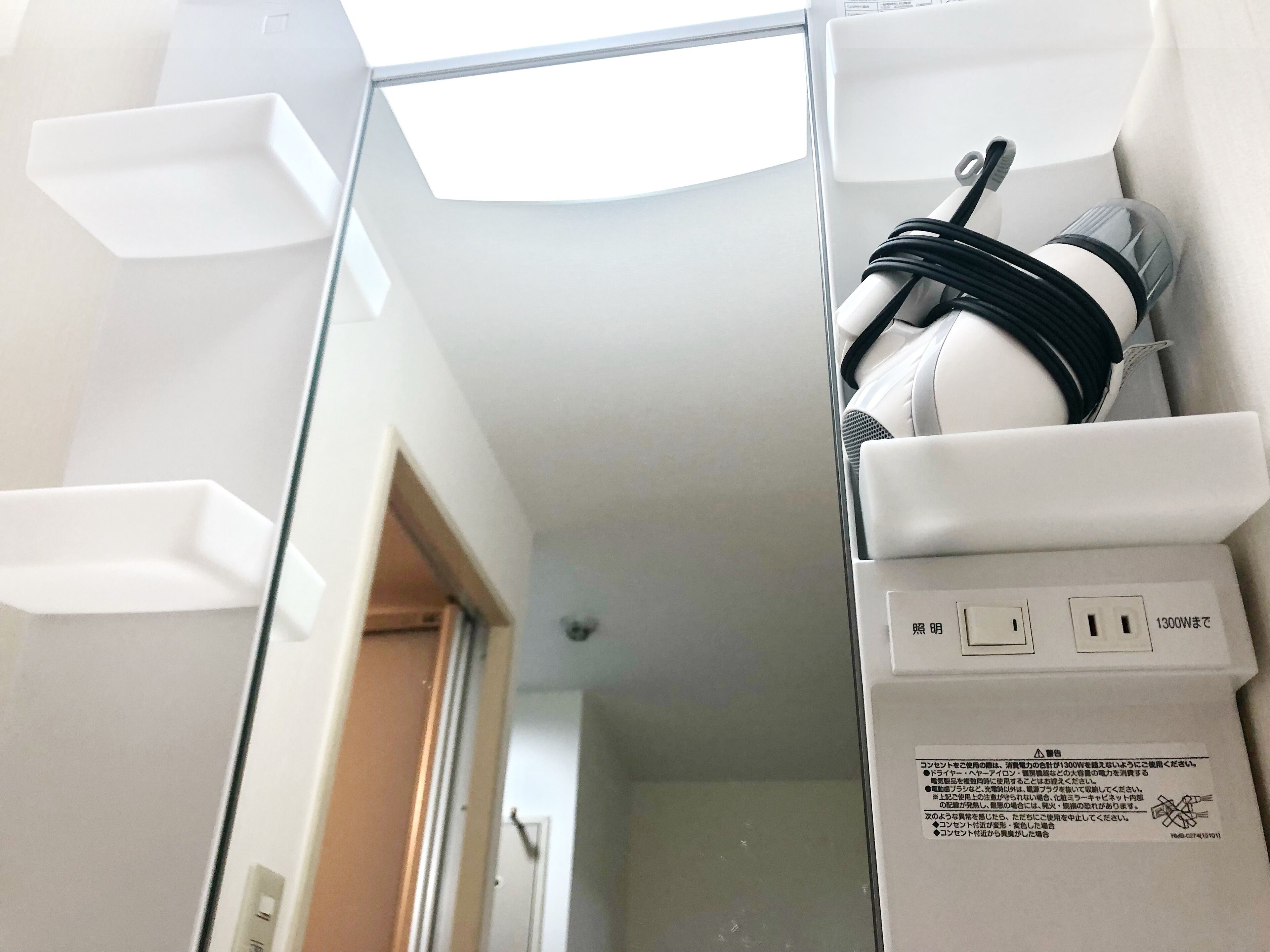 A white electrical outlet with a black cable plugged in, a white wall, and a door leading to another room.