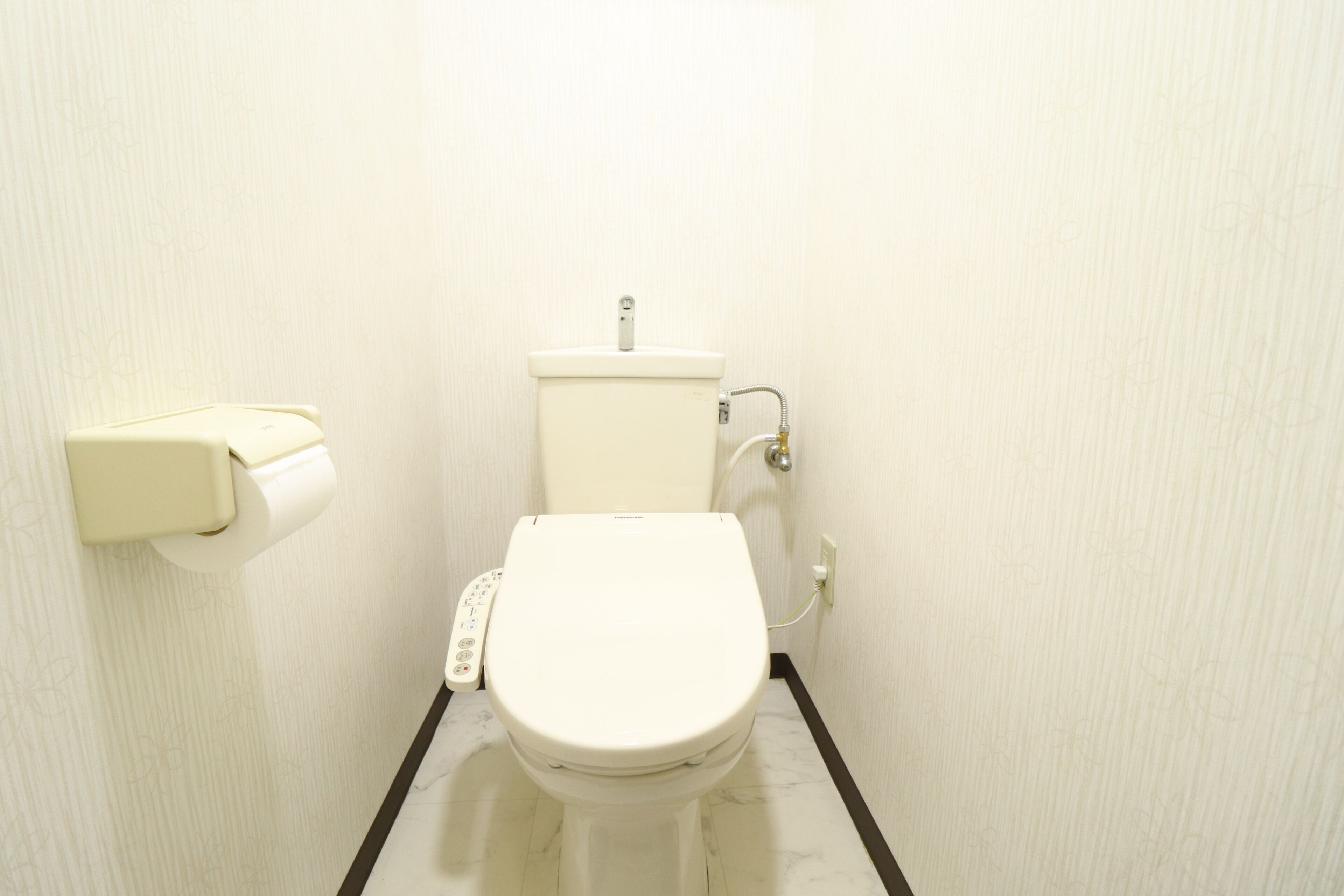 A small, white bathroom with a toilet, a paper towel dispenser, and a wall-mounted faucet.